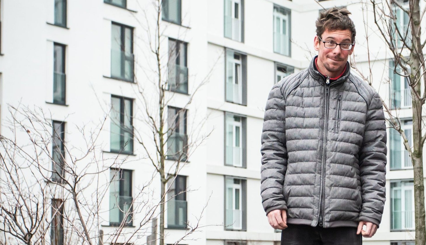 Ein Spieler der Boule Gruppe Baaken Bande in einer warmen Jacke. Im Hintergrund ein Wohnhaus in der HafenCity.