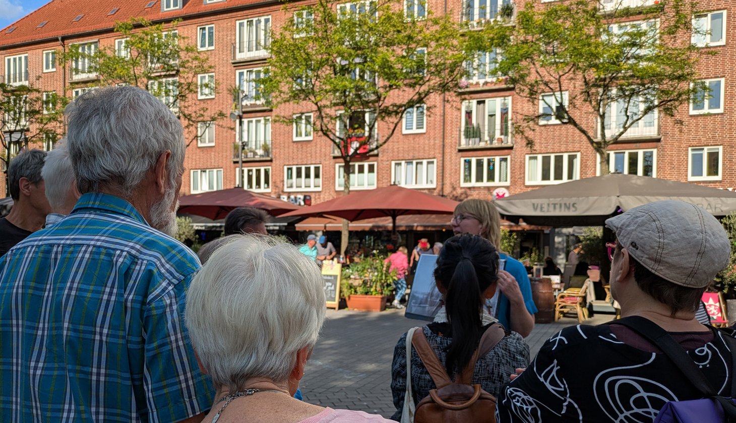 Eine Gruppe Menschen steht im Halbkreis um die Stadtführerin, die etwas in der Hand hält.