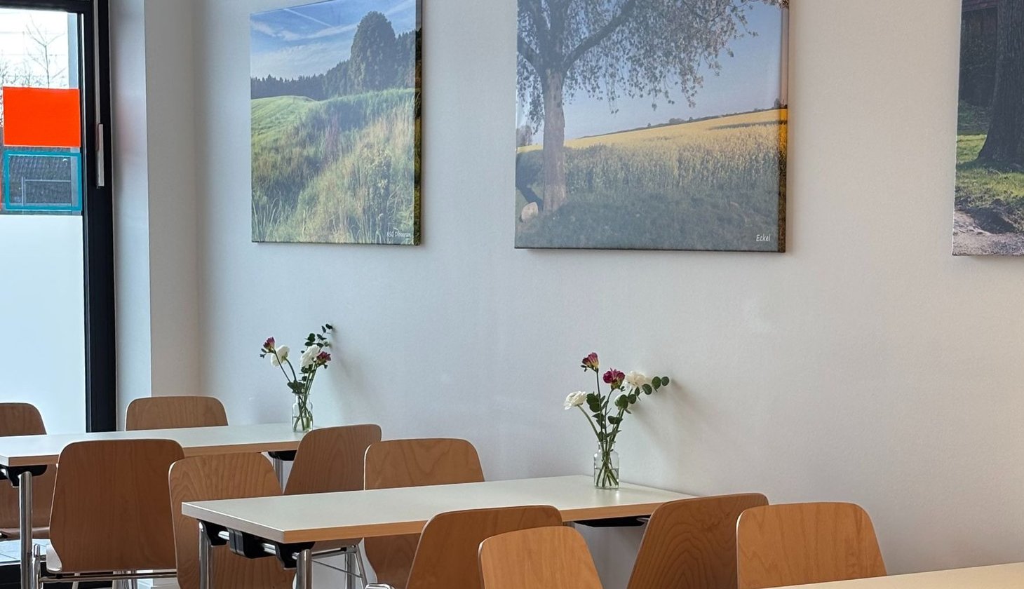 Innenraum der Assistenz, viele Tische mit Blumenvasen, Naturfotos hängen an der Wand