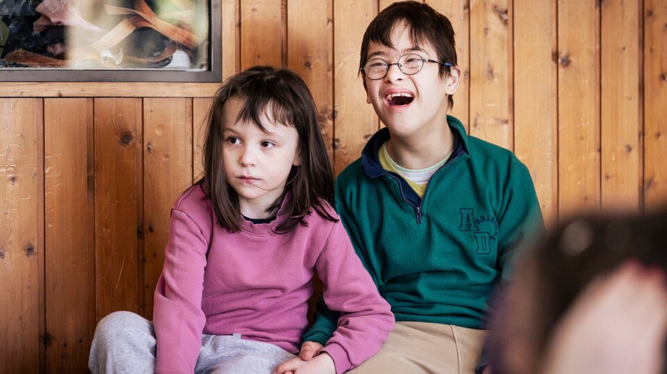 Zwei Schüler*innen der schulischen Ganztagsbetreuung sitzen nebeneinander und verfolgen aufmerksam das Hip-Hop-Angebot während der Ferienbetreuung des Sozialkontors.