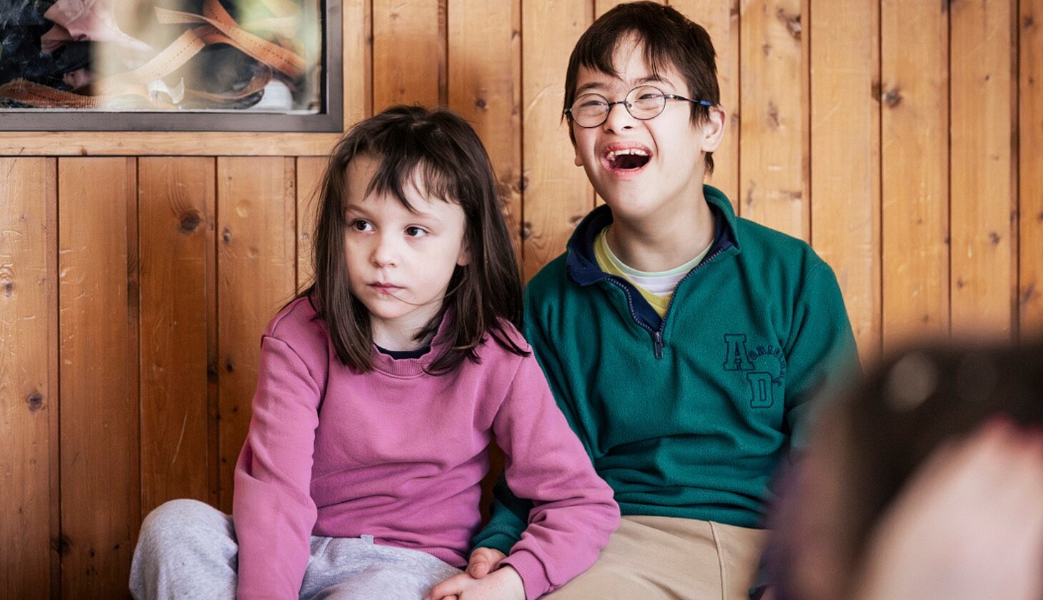 Zwei Schüler*innen der schulischen Ganztagsbetreuung sitzen nebeneinander und verfolgen aufmerksam das Hip-Hop-Angebot während der Ferienbetreuung des Sozialkontors.