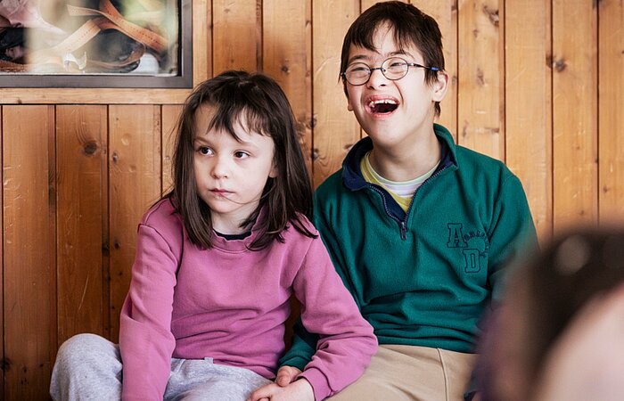 Zwei Schüler*innen der schulischen Ganztagsbetreuung sitzen nebeneinander und verfolgen aufmerksam das Hip-Hop-Angebot während der Ferienbetreuung des Sozialkontors.