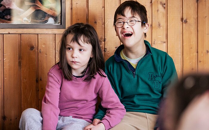 Zwei Schüler*innen der schulischen Ganztagsbetreuung sitzen nebeneinander und verfolgen aufmerksam das Hip-Hop-Angebot während der Ferienbetreuung des Sozialkontors.
