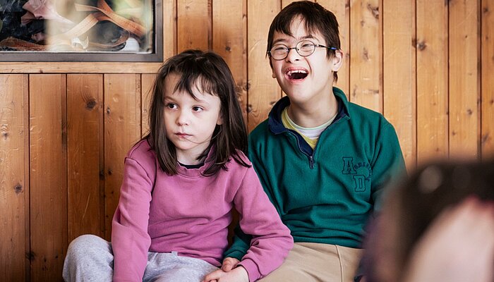 Zwei Schüler*innen der schulischen Ganztagsbetreuung sitzen nebeneinander und verfolgen aufmerksam das Hip-Hop-Angebot während der Ferienbetreuung des Sozialkontors.