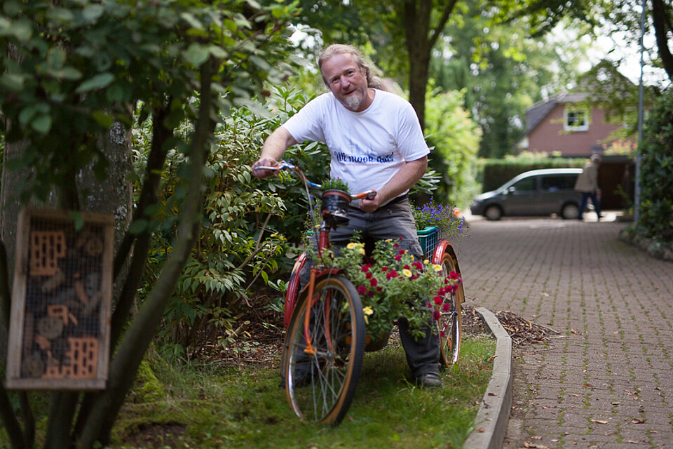 Ein Mann auf einem kleinen Fahrrad an dem Blumen hängen.