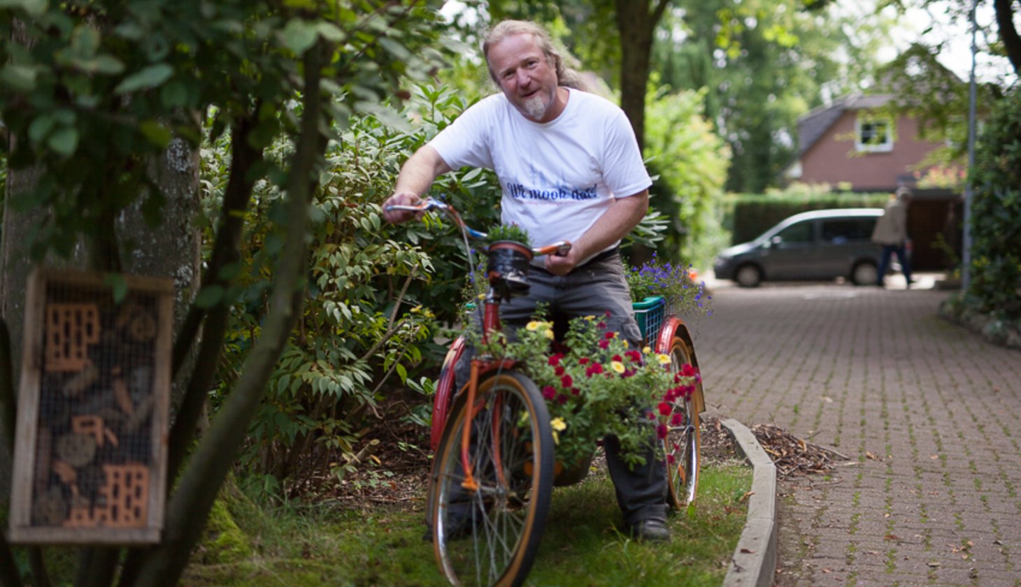 Ein Mann auf einem kleinen Fahrrad an dem Blumen hängen.