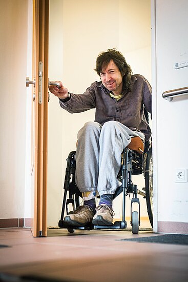 Mann im Rollstuhl öffnet eine Tür 
