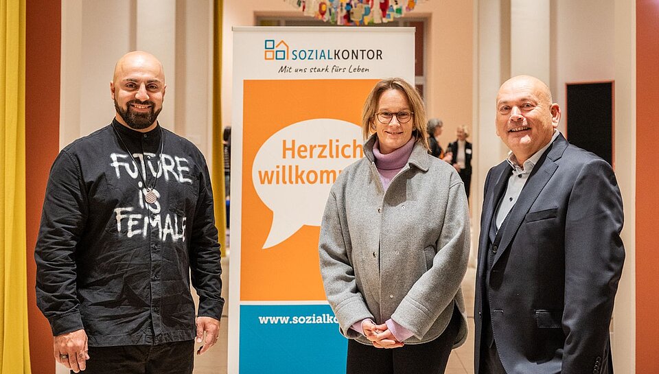 Ali Mahlodji, Melanie Schlotzhauer und Kay Nernheim (von links) bei der Netzwerkveranstaltung stehen lächelnd vor einem Banner mit der Aufschrift