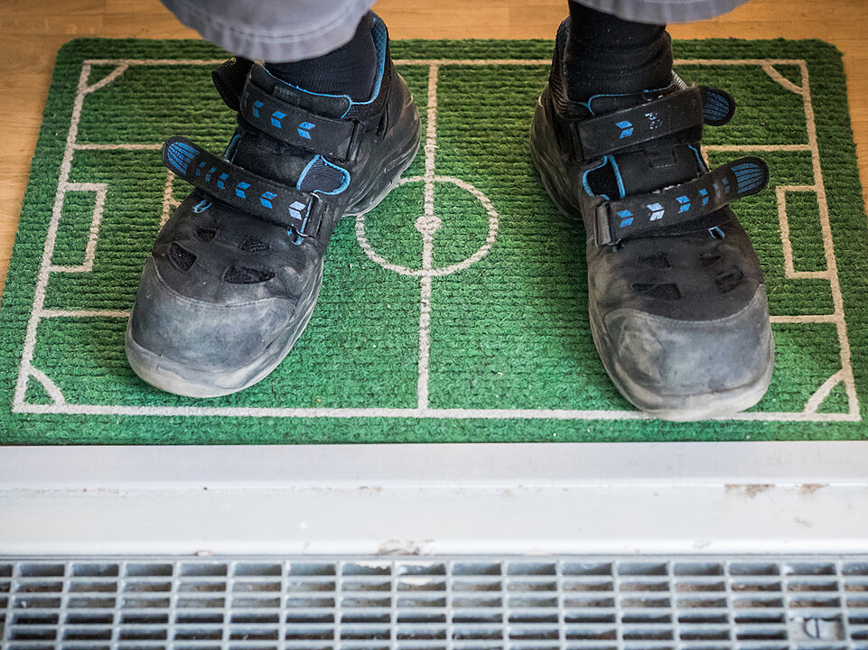 Ein Paar Schuhe steht auf einer Fußmatte, die wie ein Fußballfeld gestaltet ist.