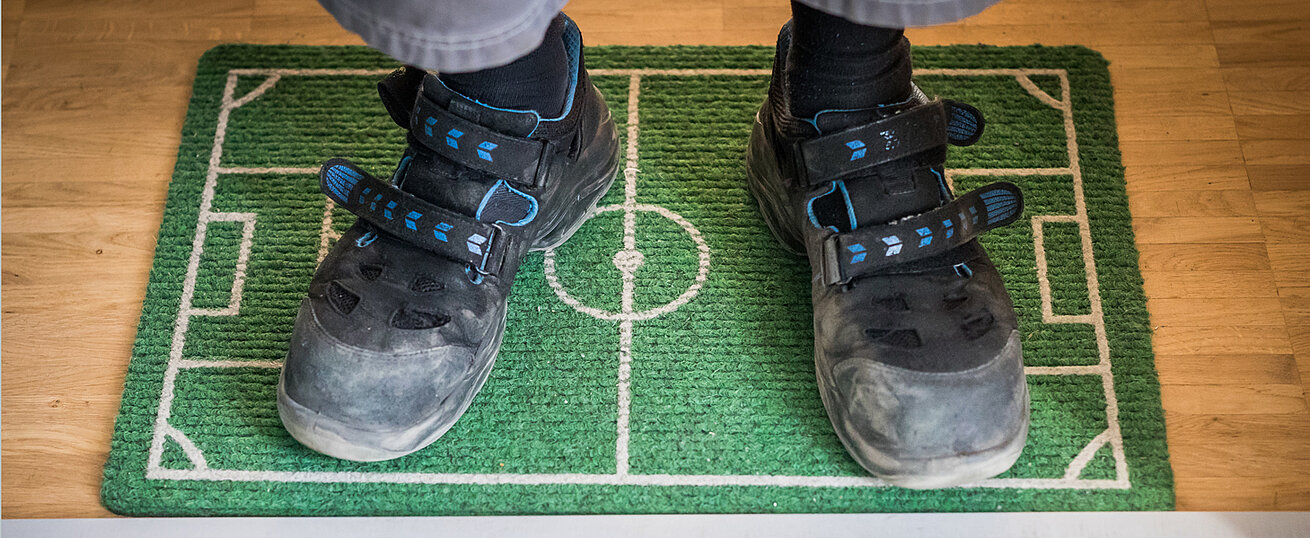 Ein Paar Schuhe steht auf einer Fußmatte, die wie ein Fußballfeld gestaltet ist.