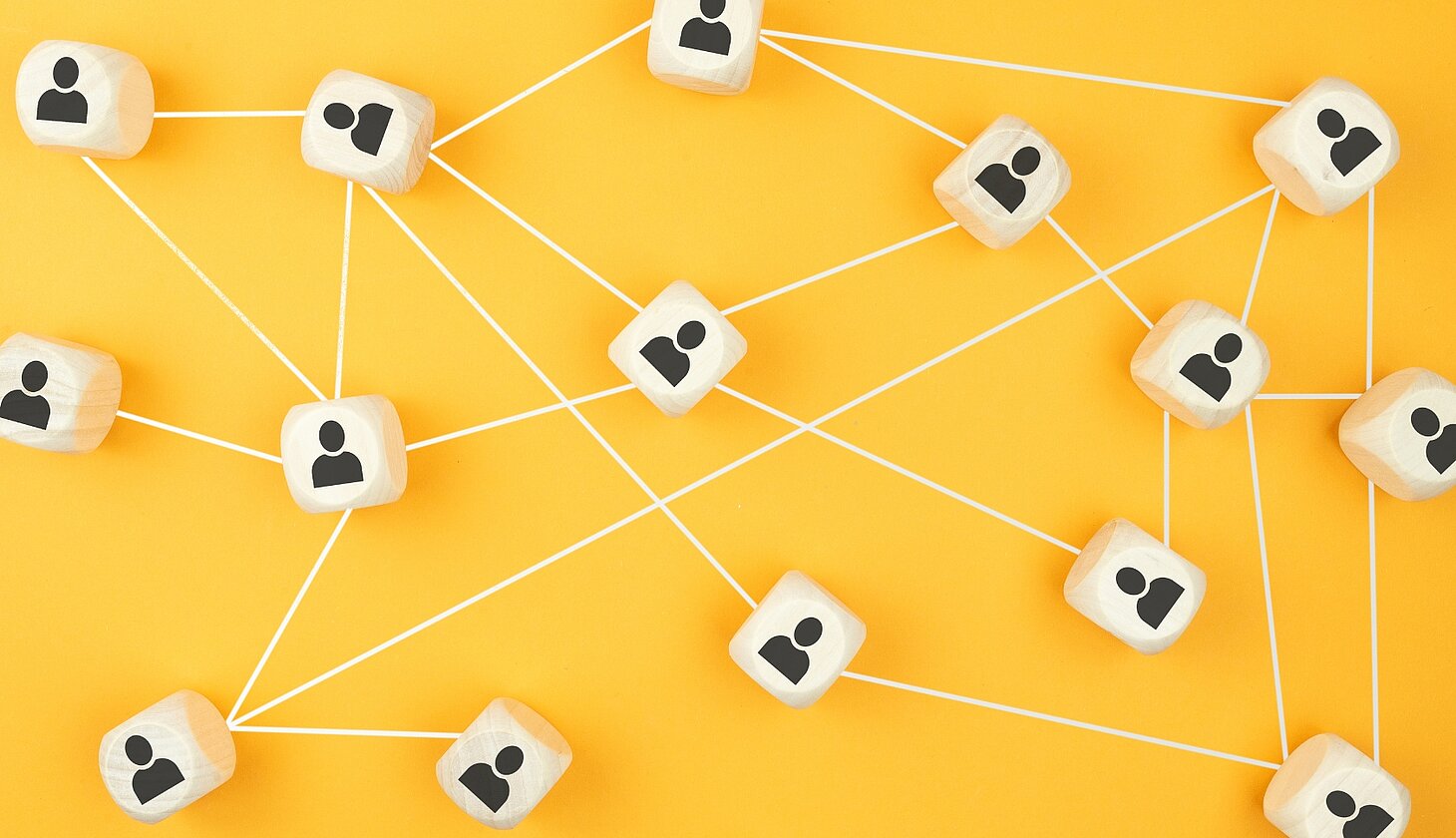 Holzwürfel mit Personen-Symbolen sind über weiße Linien auf gelbem Hintergrund miteinander verbunden und visualisieren ein Netzwerk aus Beziehungen und Kooperationen.