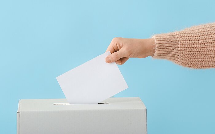 Eine Person steckt einen Stimmzettel in eine Wahlurne.