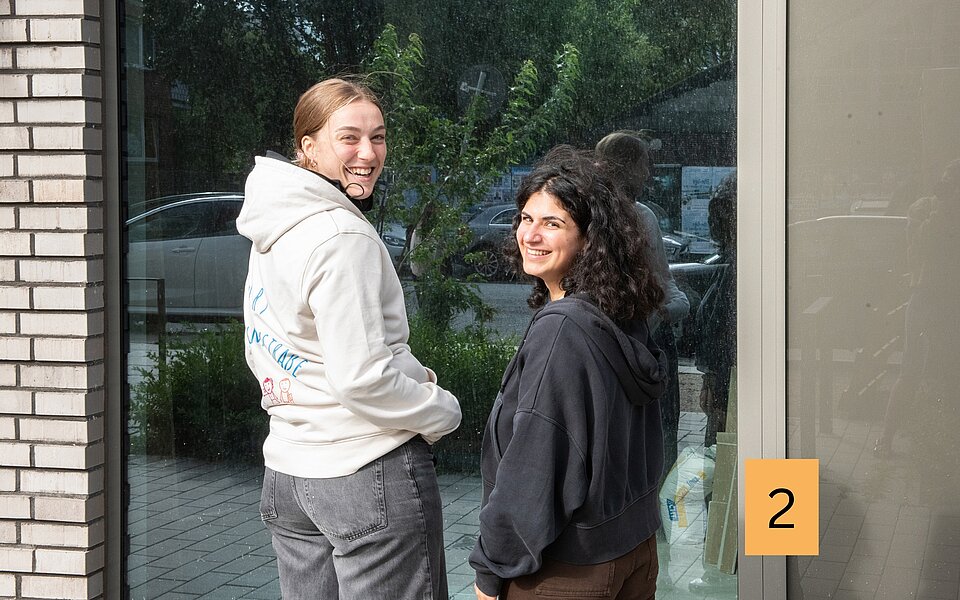Zwei Mitarbeiterinnen des Sozialkontors stehen vor der großen Fensterfront der künftigen Räume des Angebots in der Marckmannstraße 59 und schauen lachend in die Kamera.