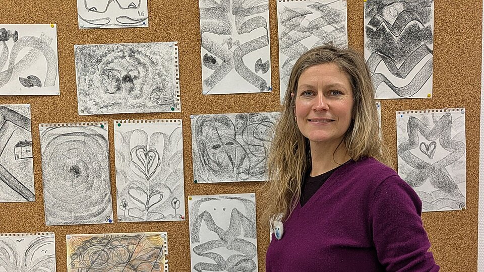 Frau steht vor ihren eigenen Kohlezeichnungen an der Pinnwand