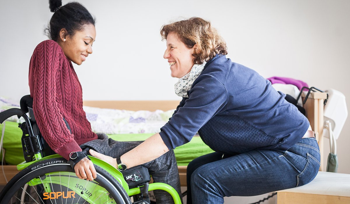 Mitarbeiterin hilft junger Frau aus dem Rollstuhl