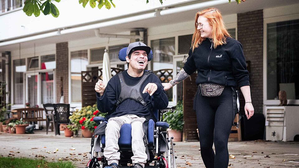 Junge Frau mit roten Haareb mit jungen Mann im Rollstuhl vor einem Gebäude