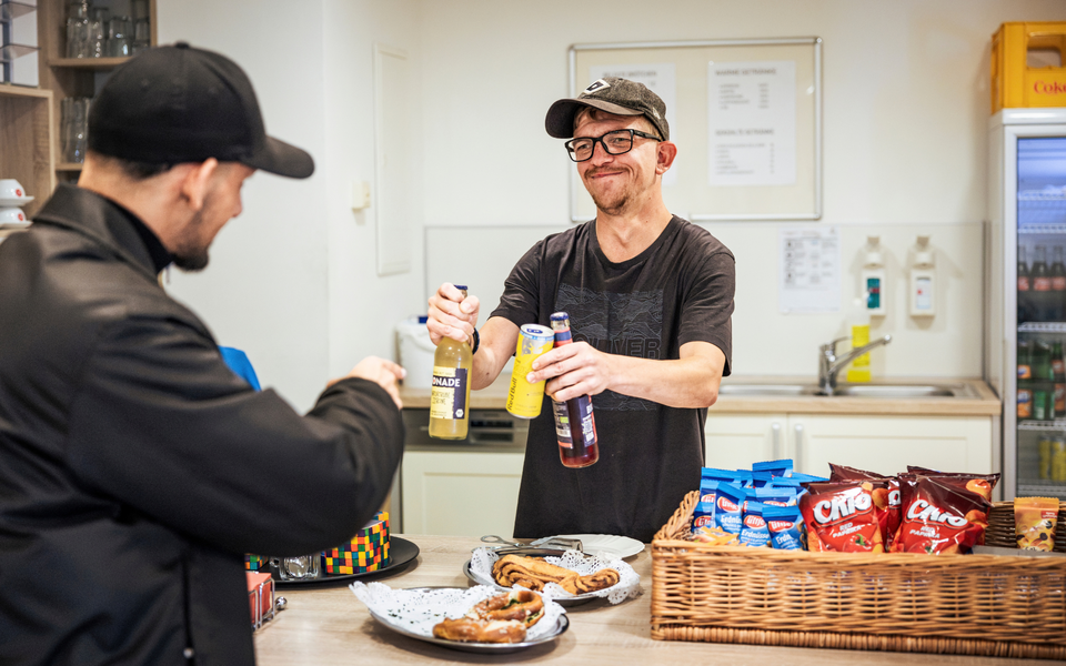 Ein Mann hinter der Theke der Cafeteria des Senator-Neumann-Hauses reicht einem Gast mehrere Getränke.