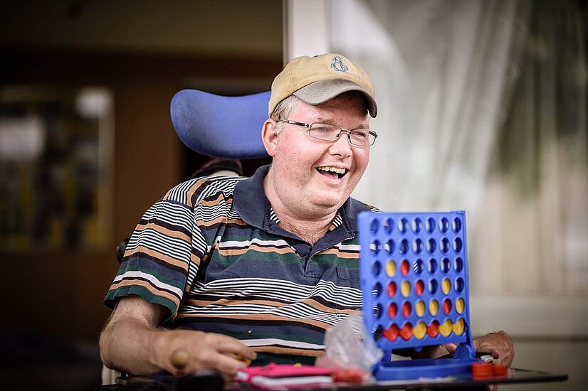 In einem Raum, Mann im Rollstuhl mit Vier-Gewinnt-Spiel