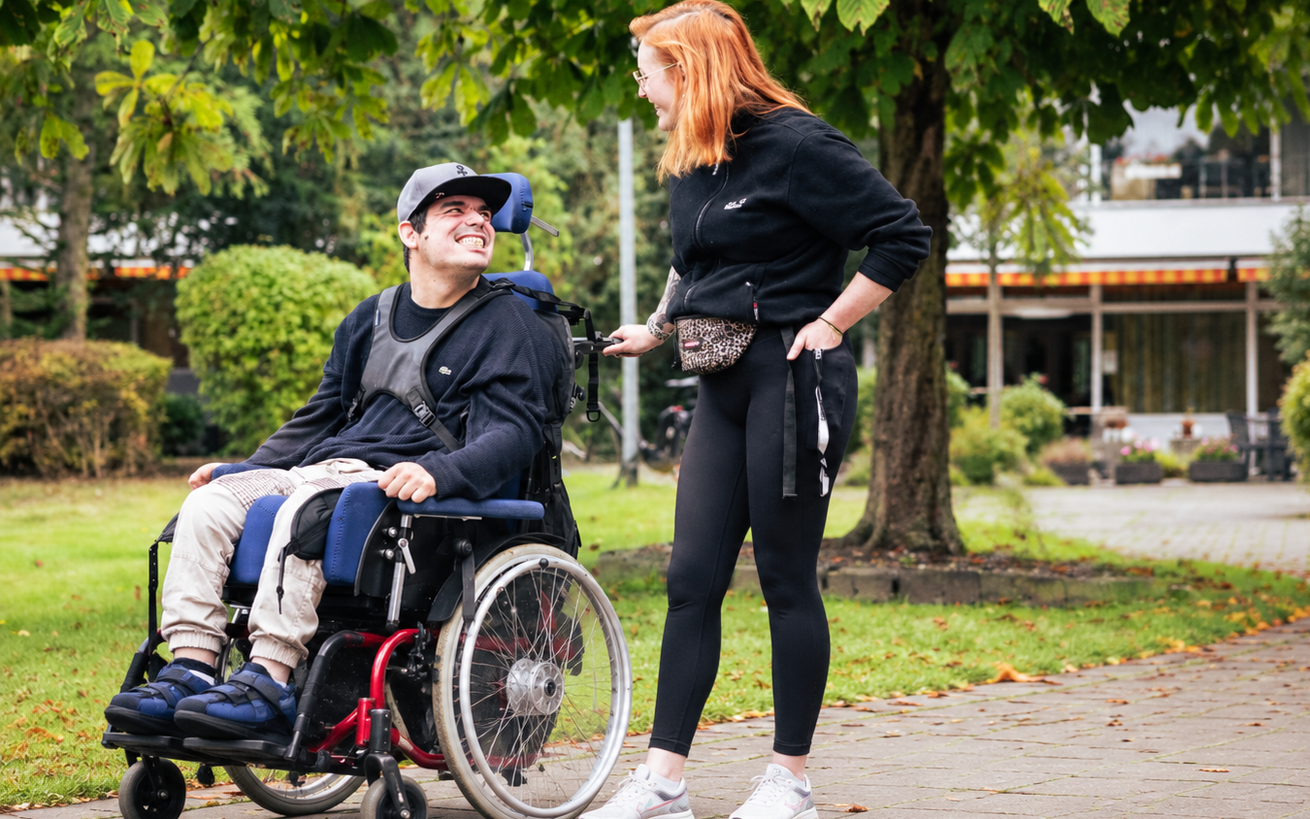 Ein Mann im Rollstuhl und eine Frau unterhalten sich lachend im Garten einer Einrichtung des Sozialkontors.