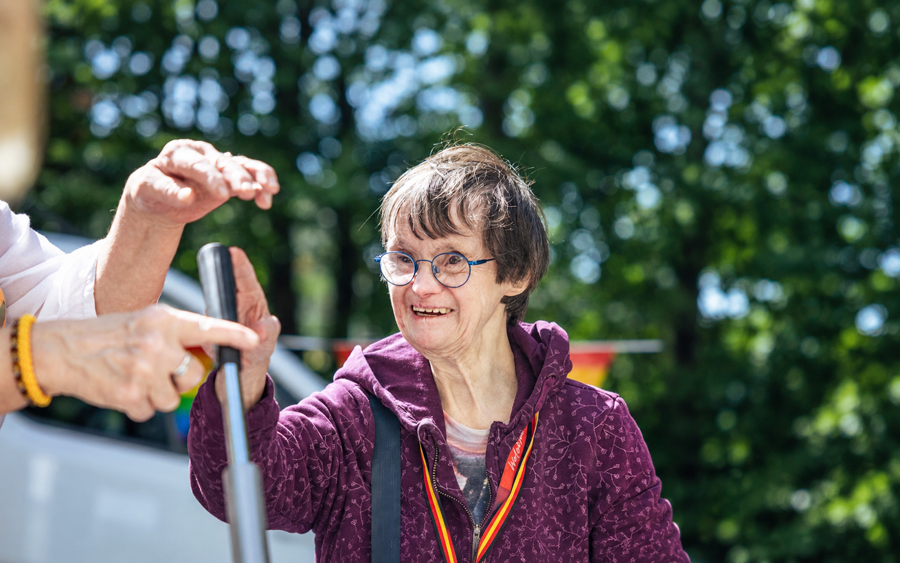 Freizeit und Bildung im Sozialkontor: Eine lächelnde Frau hält im Freien einen Griff fest. Eine weitere Person zeigt darauf.