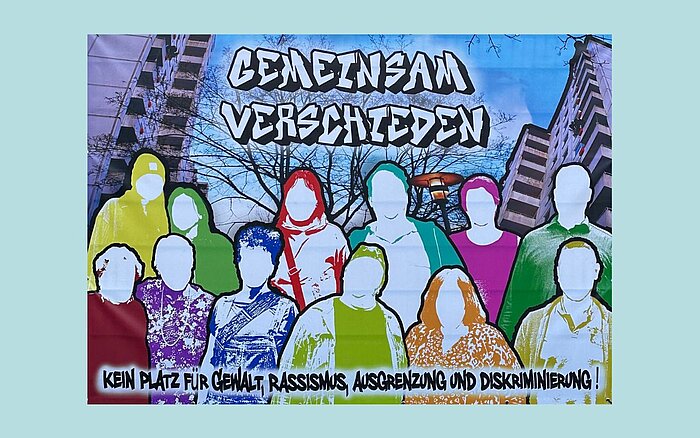 Graffiti-ähnliches Wandbild mit vielen bunten, stilisierten Menschen ohne erkennbare Gesichtszüge. Oben steht „Gemeinsam verschieden“, unten: „Kein Platz für Gewalt, Rassismus, Ausgrenzung und Diskriminierung!“. Im Hintergrund sind Wohngebäude zu sehen.