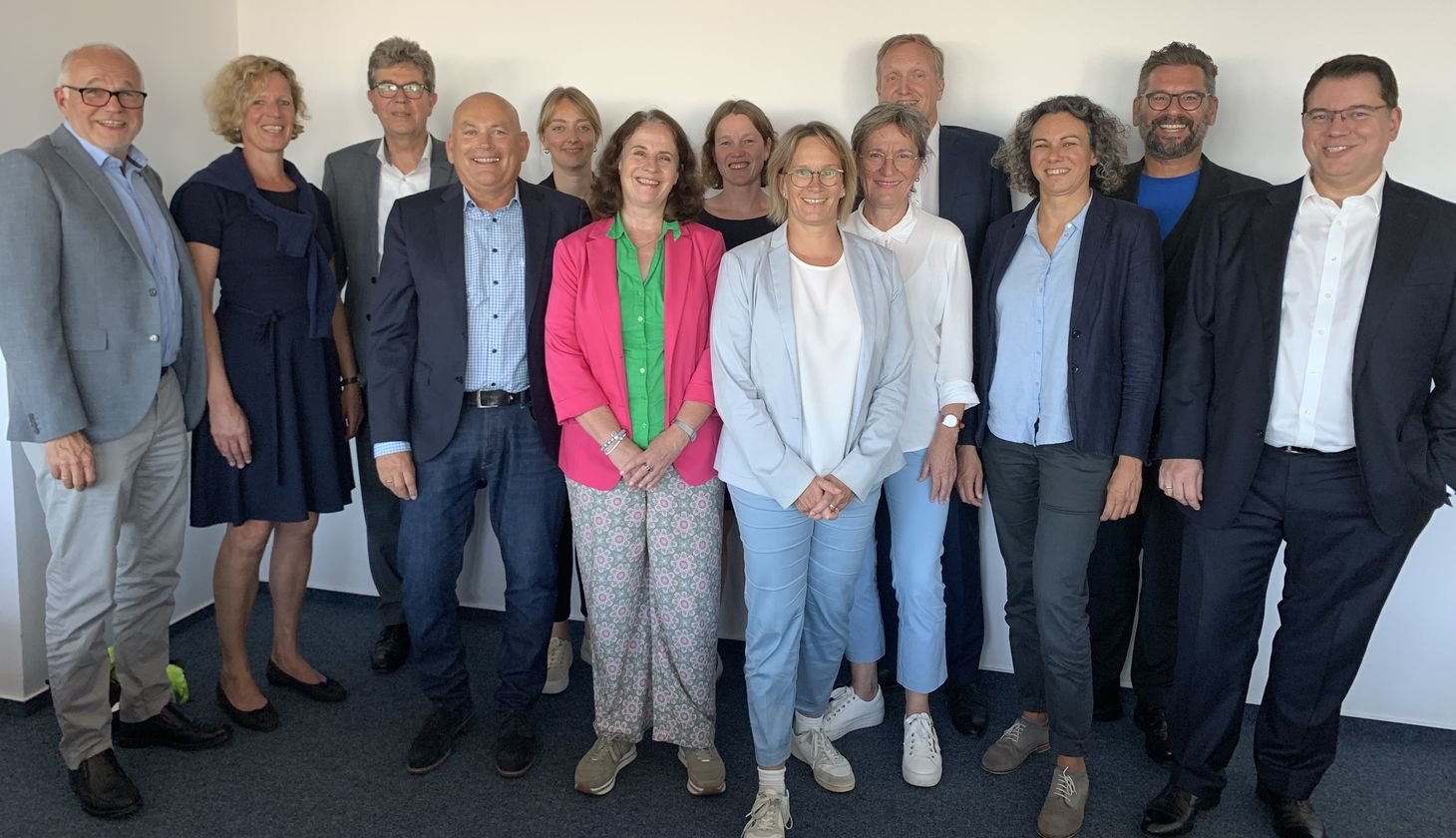 Eine Gruppe von 13 Erwachsenen in Berufskleidung posiert gemeinsam für ein Foto in einer Büroumgebung.