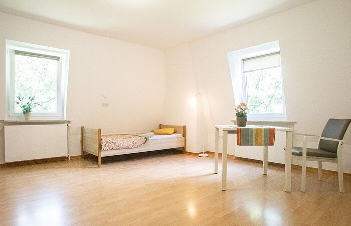 Ein lichtdurchflutetes Zimmer mit Bett, Tisch, Stuhl und zwei Fenstern im Haus Eckel, einer Einrichtung des Sozialkontors für Menschen mit geistigen Einschränkungen.