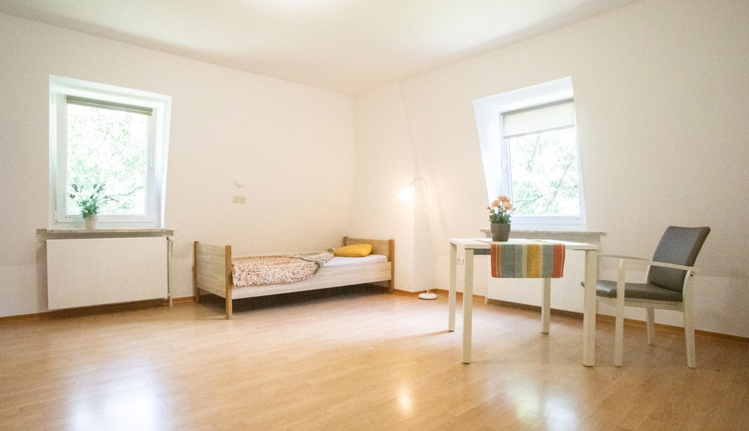 Ein lichtdurchflutetes Zimmer mit Bett, Tisch, Stuhl und zwei Fenstern im Haus Eckel, einer Einrichtung des Sozialkontors für Menschen mit geistigen Einschränkungen.