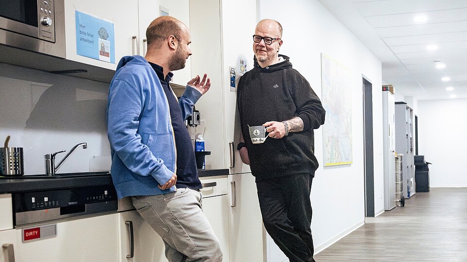 Niklas Luy und ein Kollege unterhalten sich in der Teeküche ihres Büros bei GUT GEFRAGT.