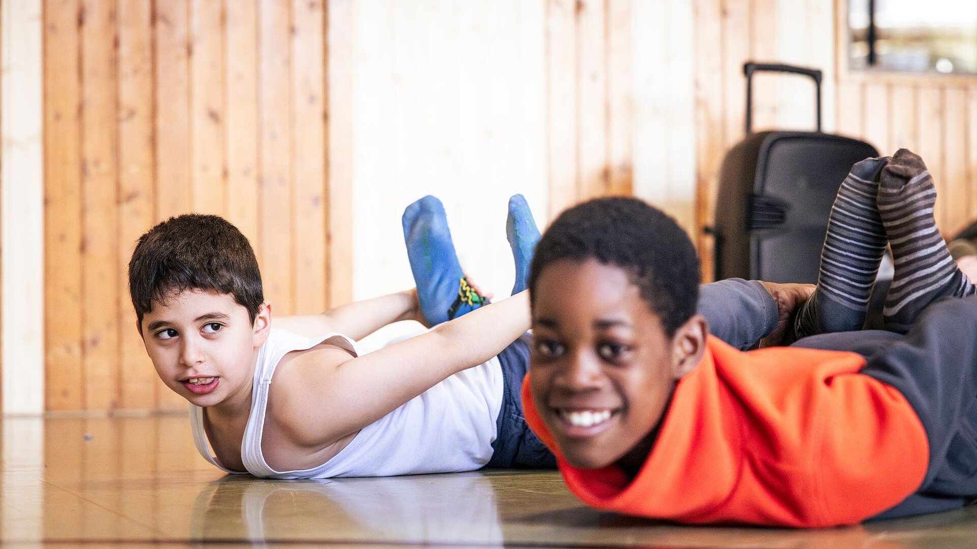 Zwei Förderschüler liegen lachend auf dem Boden einer Turnhalle und machen eine Bewegungsübung.