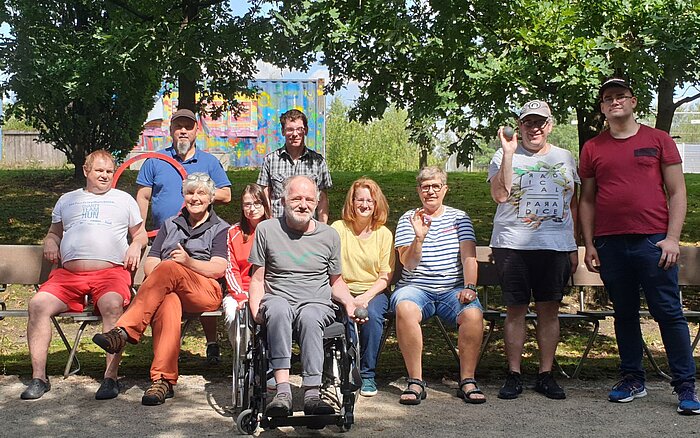 Zehn Erwachsene verschiedenen Alters in sommerlicher Freizeitkleidung. Ein Mann sitzt im Rollstuhl. Das ist die Boule-Gruppe Baaken Bande vom Sozialkontor im Lohsepark in Hamburg.