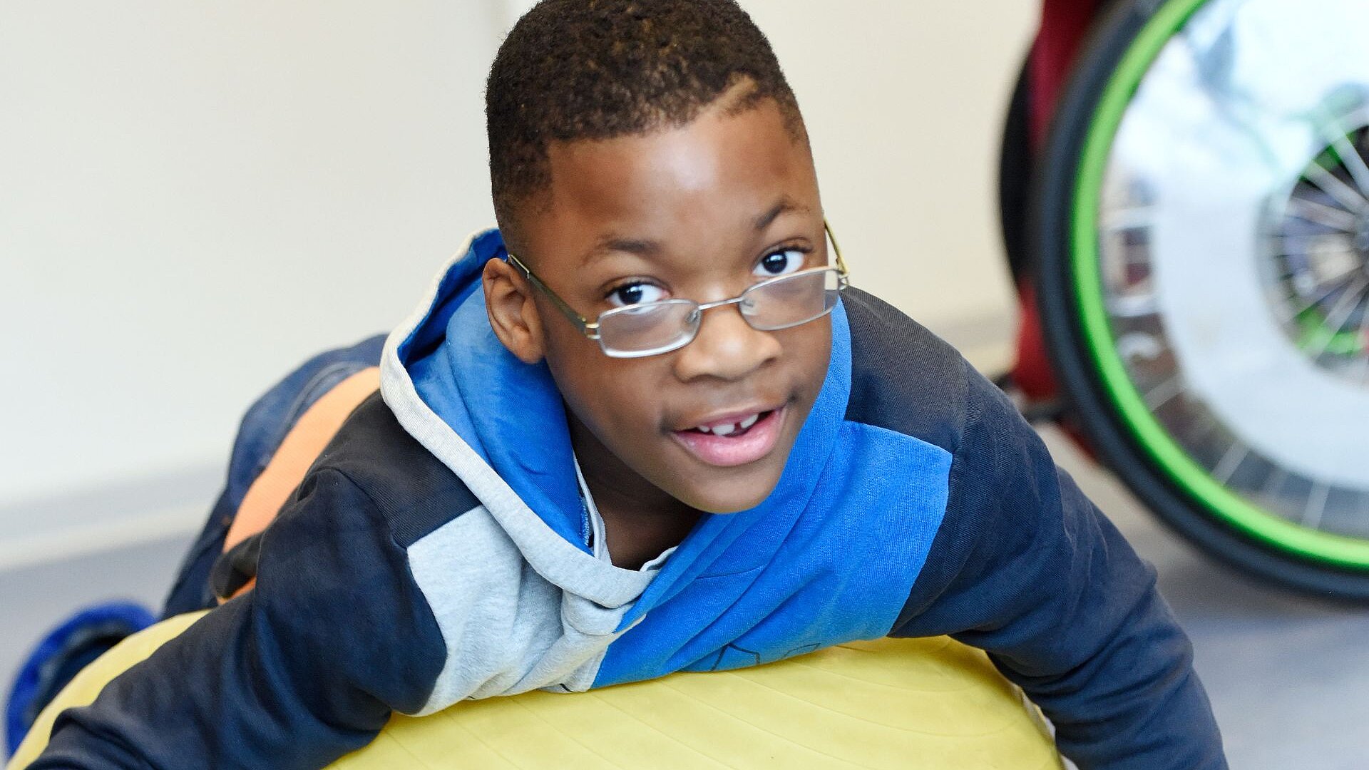 Förderschüler mit Brille liegt lächelnd auf einem großen Gymnastikball.