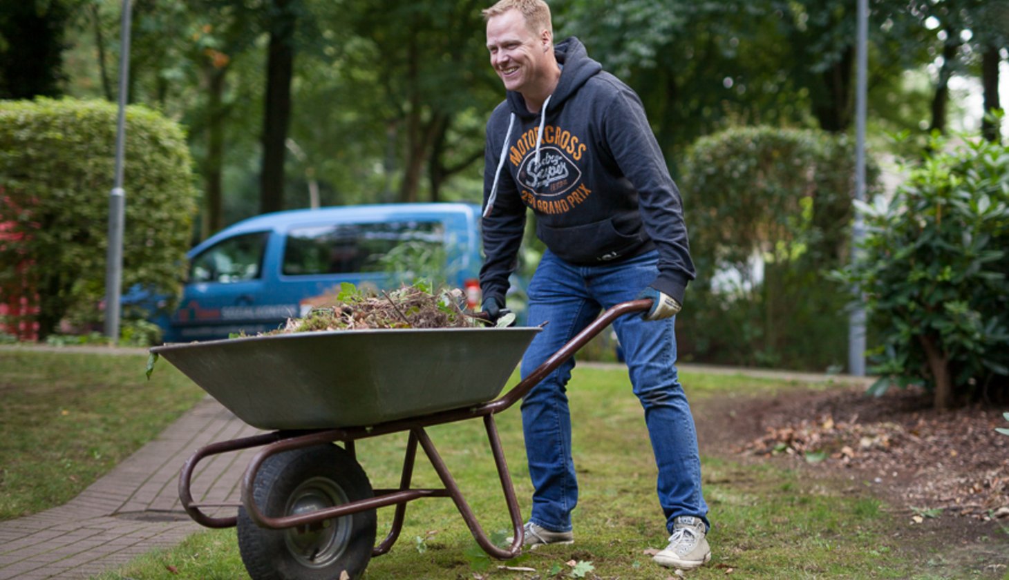 Ein Mann mit einer Schubkarre in der sich Erde und Unkraut befindet.