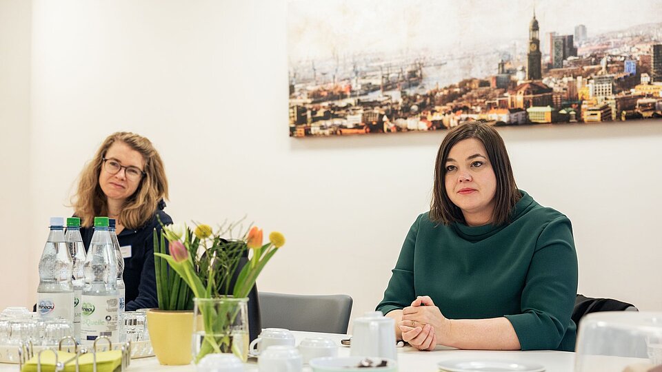 Hamburgs Zweite Bürgermeisterin Katharina Fegebank (rechts) sitzt an einem Tisch, neben ihr Britt Viemann (links), die Mietersprecherin von Wohnen mit Assistenz Klotzenmoor, einem Wohn-Angebot des Sozialkontors