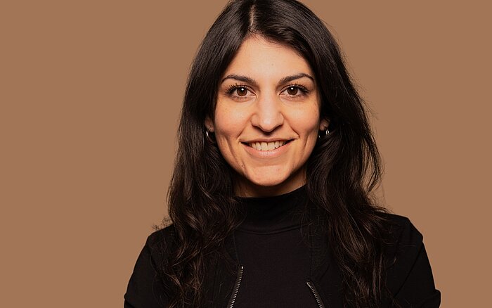 Zamina Ahmad von shades&contrast vor einem einfarbigem, beigen Hintergrund.