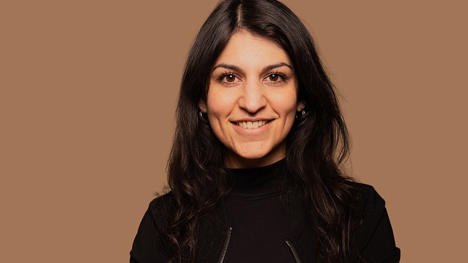 Zamina Ahmad von shades&contrast vor einem einfarbigem, beigen Hintergrund.