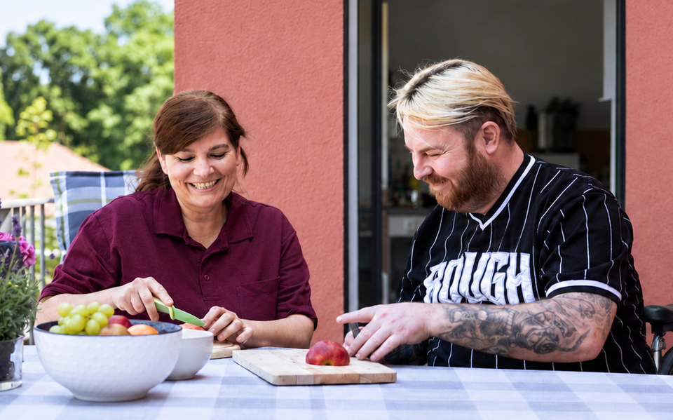 Mit uns stark fürs Leben – Sozialkontor: Eine Frau und ein Mann bereiten gemeinsam Obst an einem Tisch auf der Terrasse vor.
