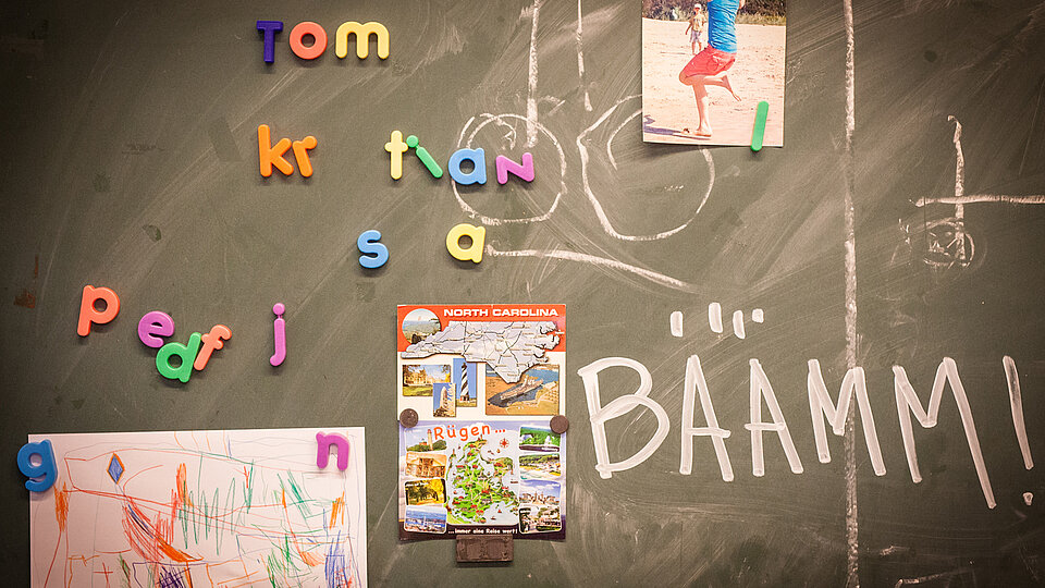 Eine bemalte Tafel mit Buchstaben-Magneten und angehängten Bildern.
