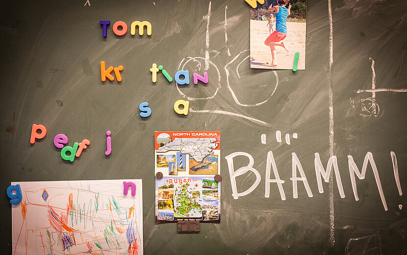 Eine bemalte Tafel mit Buchstaben-Magneten und angehängten Bildern.