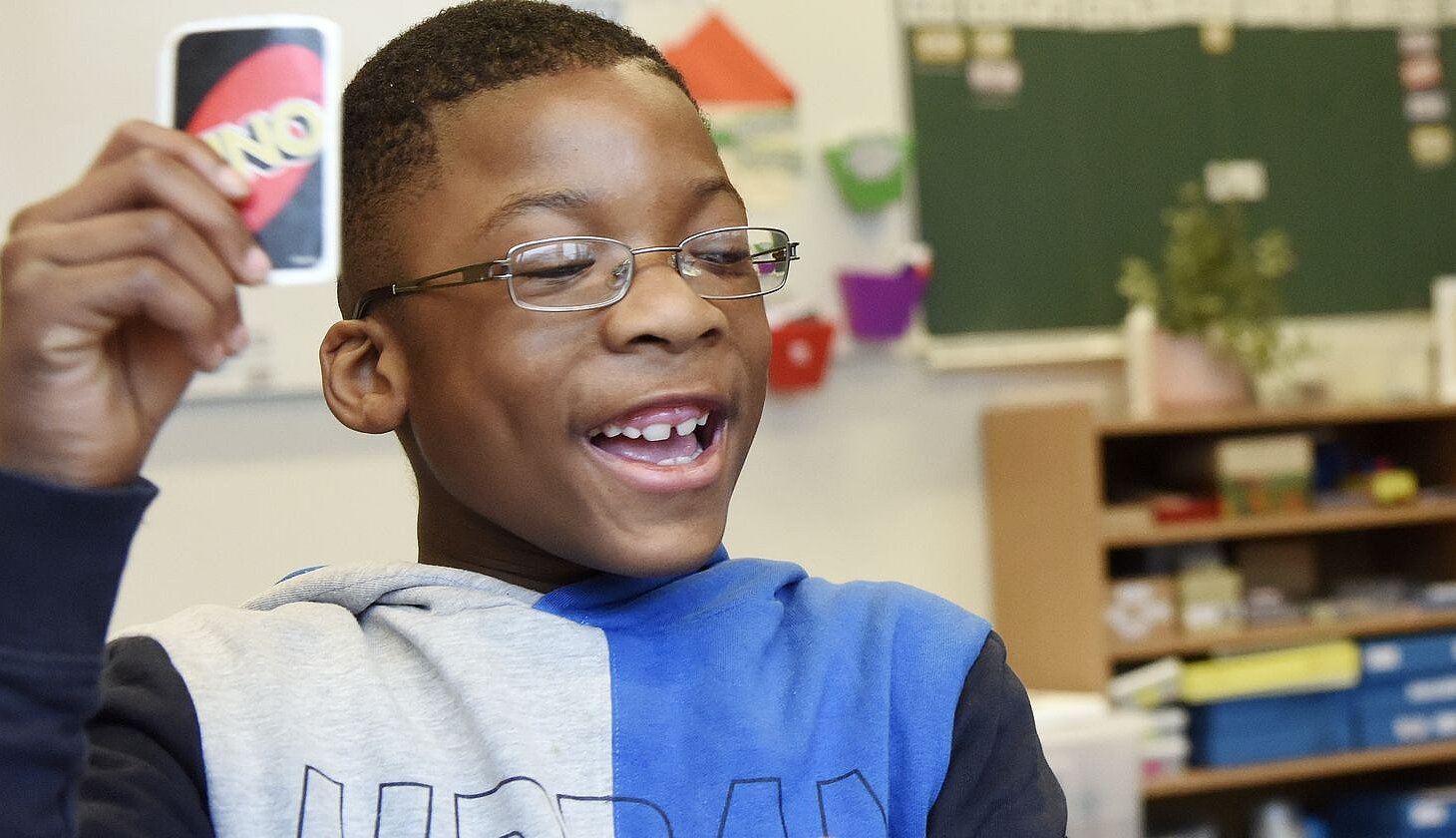 Ein Junge in der Schule lacht und hält während eines Spiels eine Uno-Karte hoch.