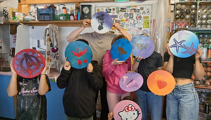 Teilnehmende des Streetart-Projekts halten ihre selbst besprühten Schallplatten mit Tier-, Herz- und Comicmotiven vor sich.