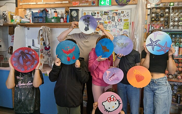 Teilnehmende des Streetart-Projekts halten ihre selbst besprühten Schallplatten mit Tier-, Herz- und Comicmotiven vor sich.