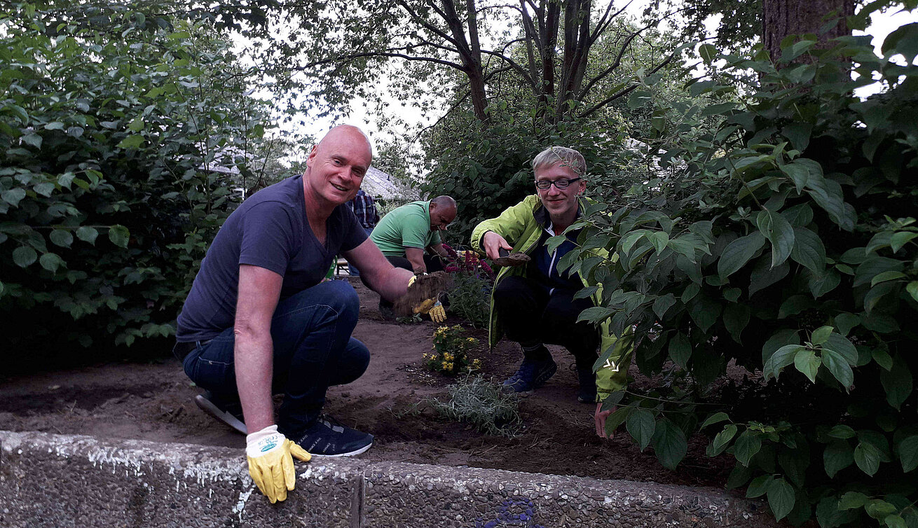 Mehrere Menschen hocken in einem Beet und vollbringen Gartenarbeit