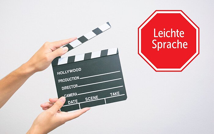 Zwei Hände halten eine schwarze Filmklappe vor einem weißen Hintergrund. Rechts daneben ist ein rotes Stoppschild mit der Aufschrift „Leichte Sprache“.