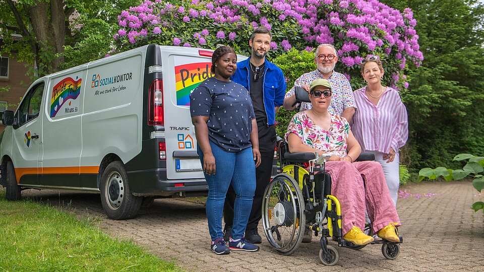 Menschen mit und ohne Behinderung stehen vor einem Pride-Tour-Fahrzeug des Sozialkontors und kommen miteinander ins Gespräch. Das Fahrzeug ist mit Regenbogenfarben gestaltet und wirbt für Vielfalt und Akzeptanz.