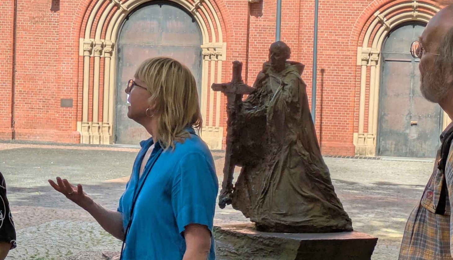 Stadtführerin vor Statue, das einen Mönch mit großem Kreuz in der Hand zeigt.