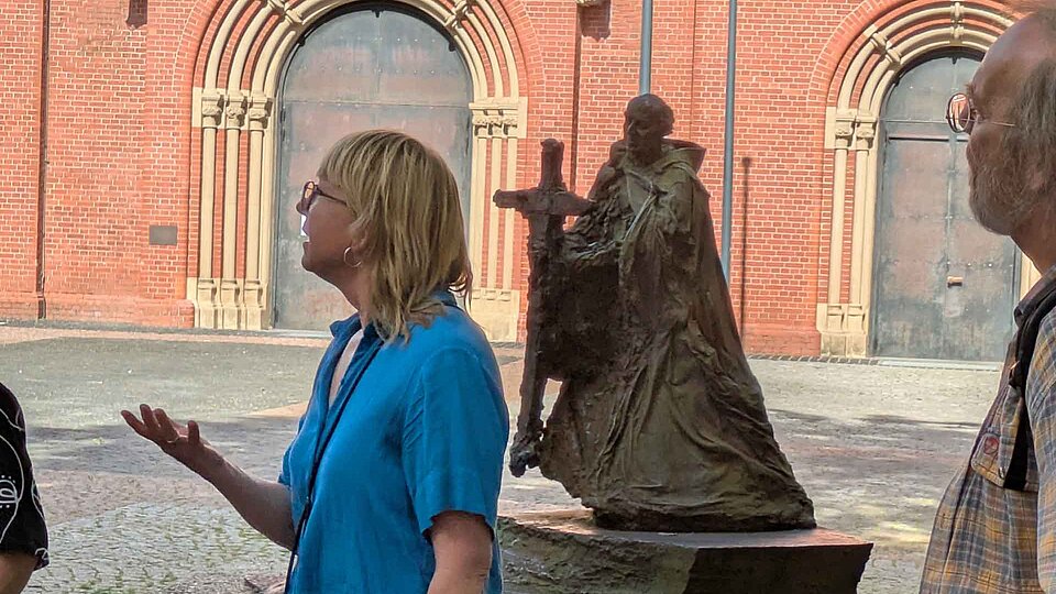 Stadtführerin vor Statue, das einen Mönch mit großem Kreuz in der Hand zeigt.