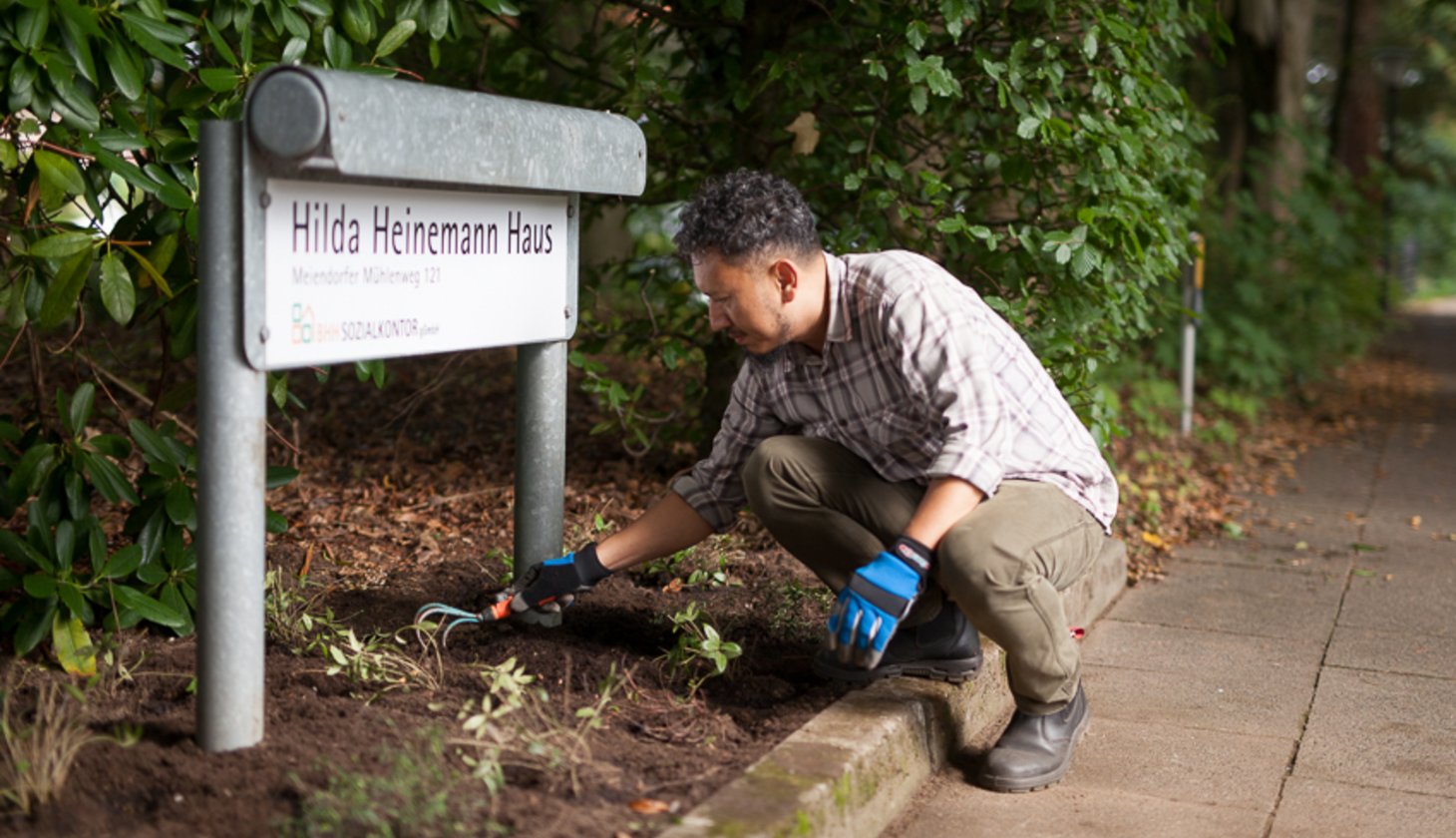 Ein Hilda-Heinemann-Haus-Schild und ein Mann der Gartenarbeit vollzieht