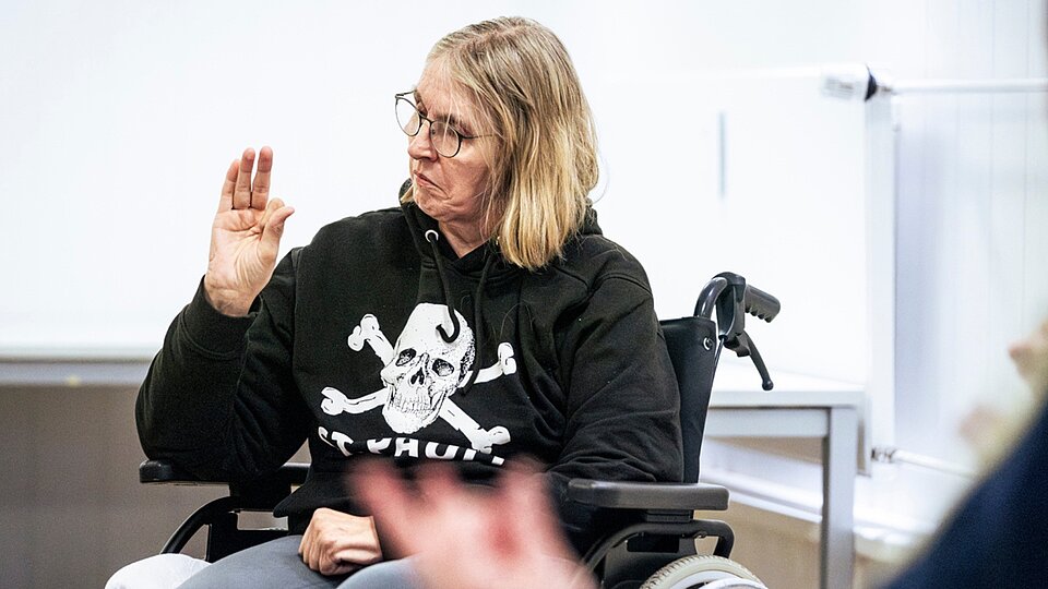 Rollstuhlnutzerin mit St.-Pauli-Pullover hebt die Hand und macht Fingerübungen im Bewegungsangebot.