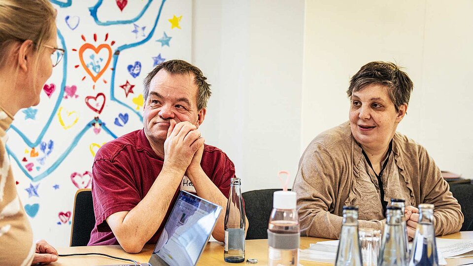 Drei Personen sitzen an einem Tisch und sprechen miteinander